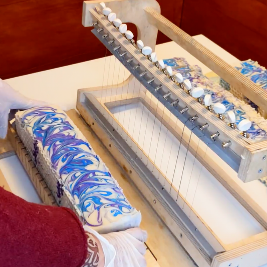 Rosemary soap with blue and purple swirls about to be cut with a wooden soap cutter.