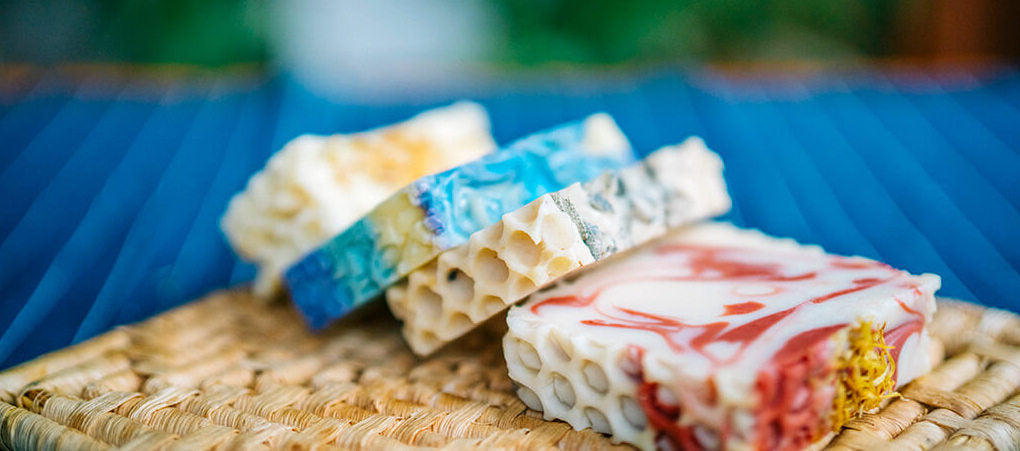 Colorful handcrafted natural honey soaps lay on a weaved grass tray.