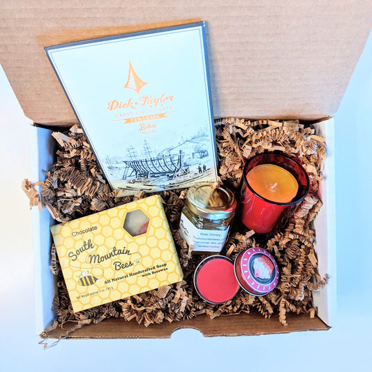 Sweet Candle Light is a gift set with a chocolate honey soap, a 2oz raw honey jar from our bees, a 100% beeswax candle for over 12 hours of glowing light in a red glass candle holder, a cherry lip gloss, and a craft chocolate bar.