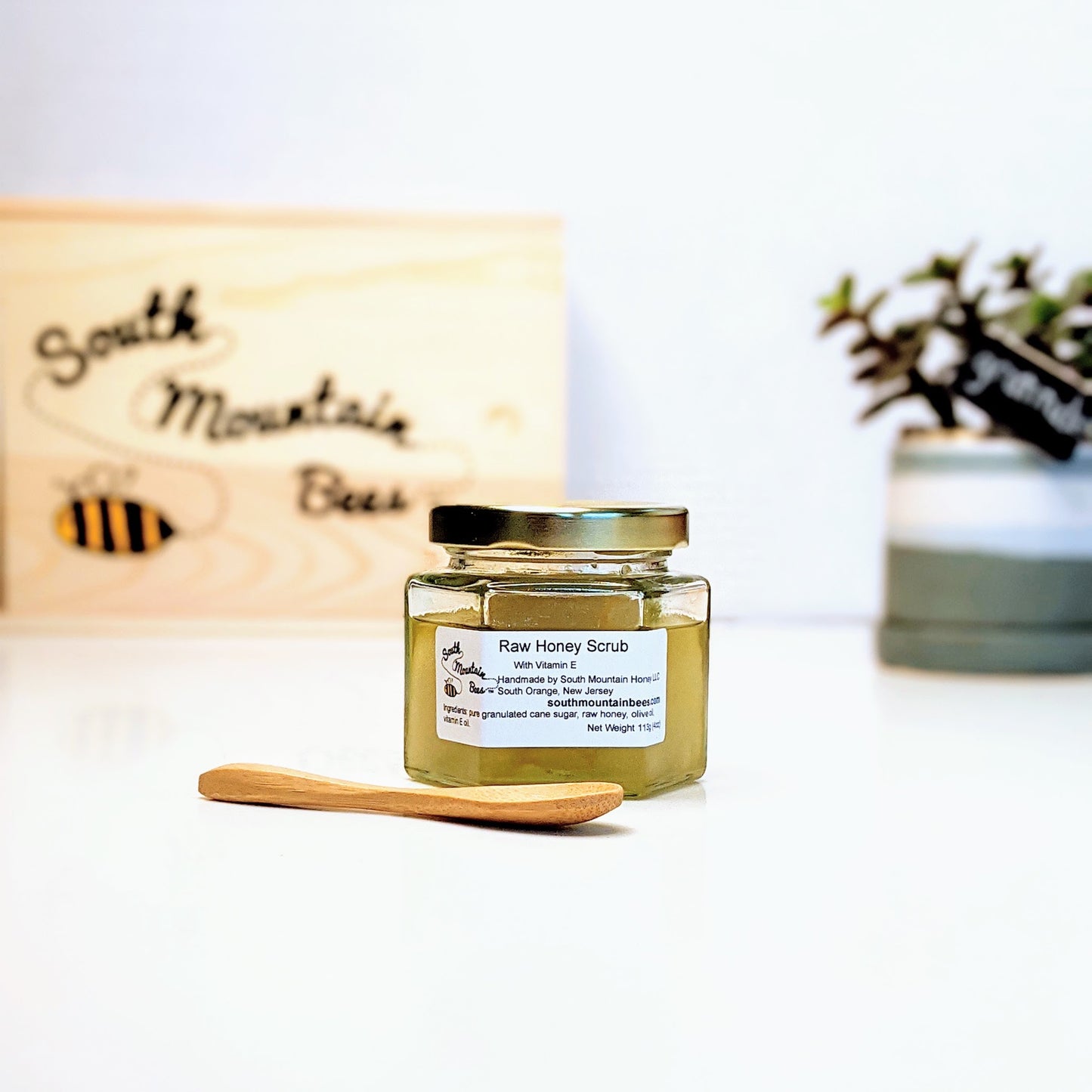 Raw honey scrub and bamboo spoon in glas hexagonal jar with gold lid.