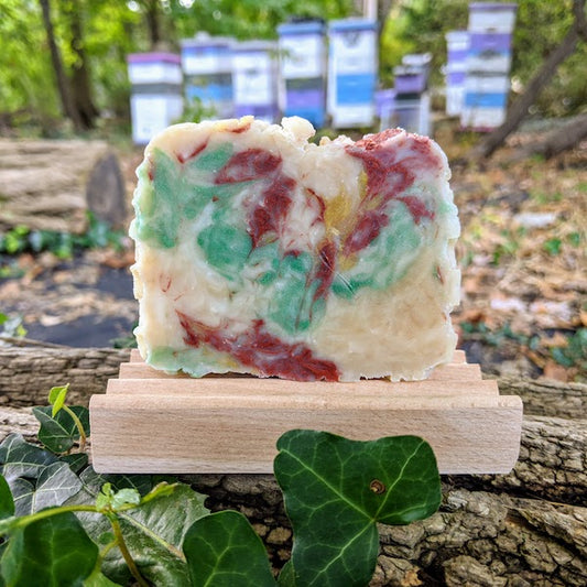 Rosemary soap with green, red and ochre swirls rests on a beech wood soap dish with beehives in the background and fall foliage all around.