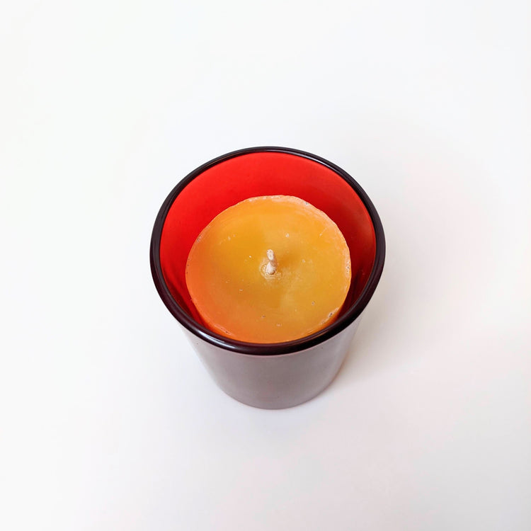 a 100% beeswax votive candle in a red glass candle holder.