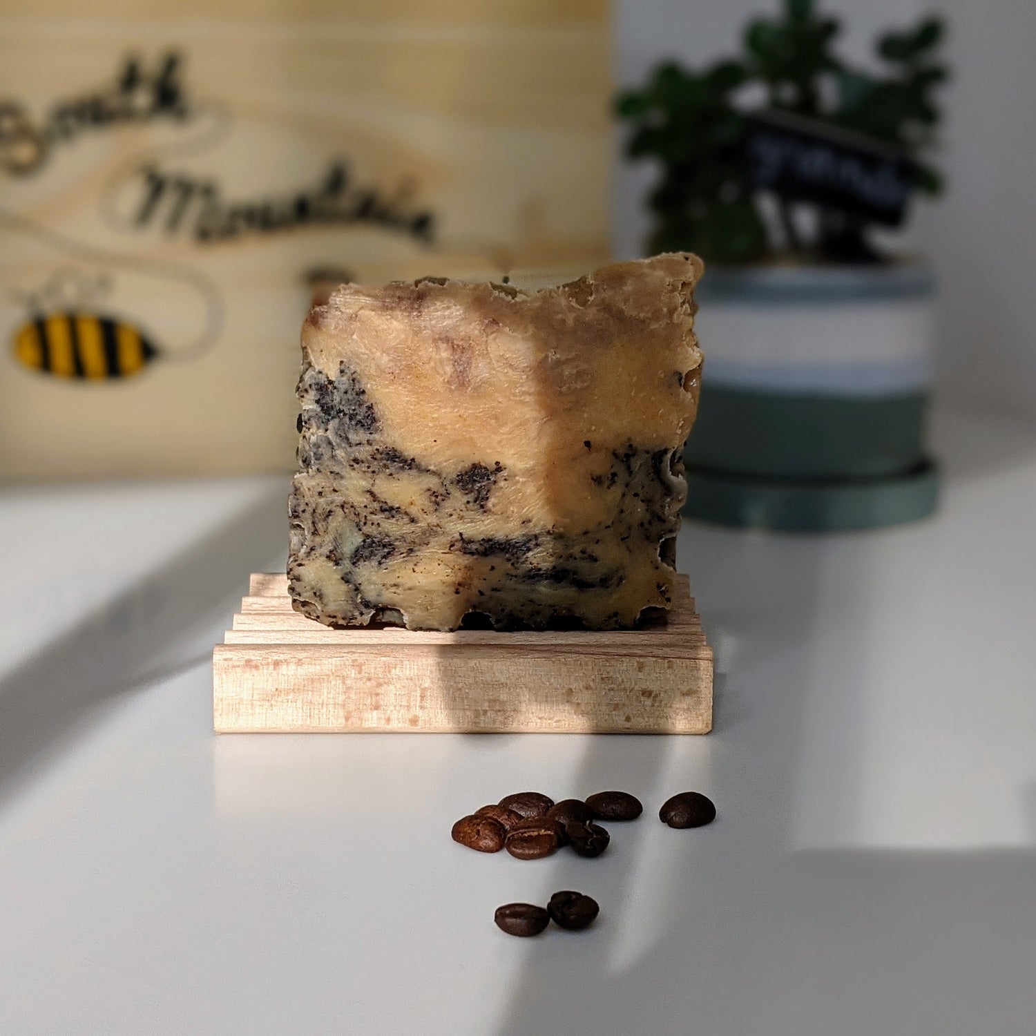 Our natural espresso soap resting on a wooden soap dish in the afternoon light.  Coffee grounds in the foreground, a succulent and a branded wooden box in the background.