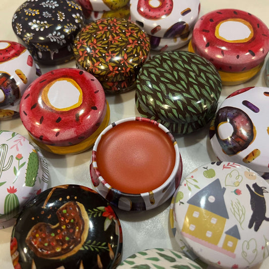 colorful lip balm tins. one is open showing lush and creamy cherry flavored lip balm.