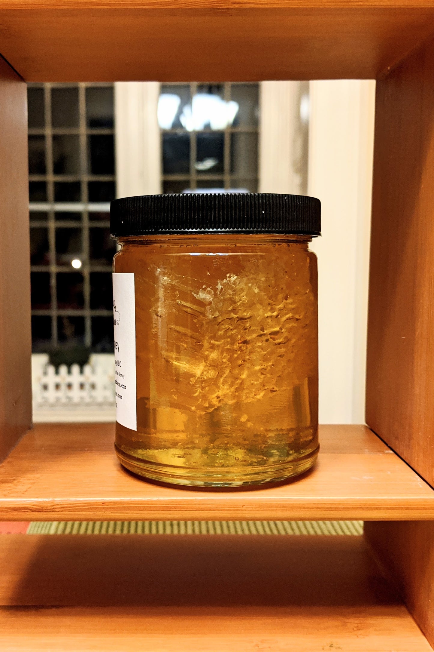 Side view of a jar of chunk honey, where you can see the honey comb inside the  liquid honey.