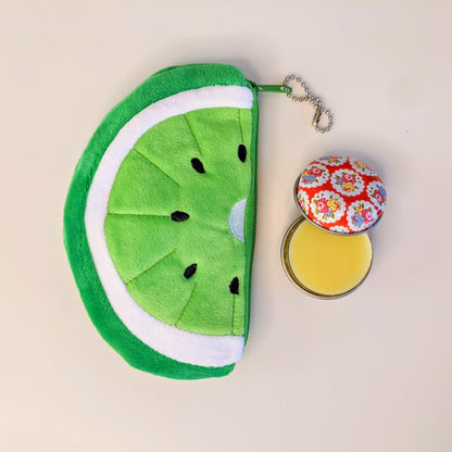 Bright  green and white melon shaped coin purse adjacent to open lip balm tin.