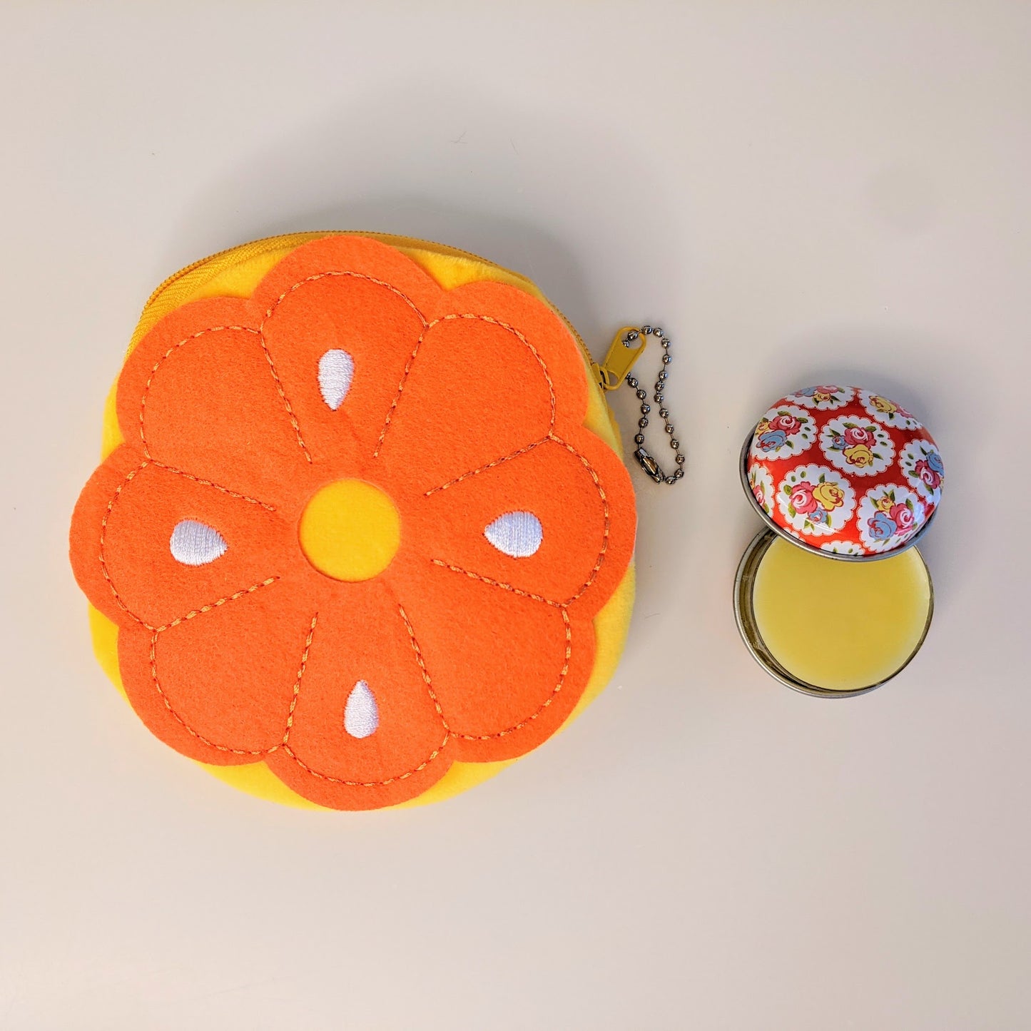 A beeswax lip balm rests open next to a bright soft plush coin purse in the shape of an orange slice.