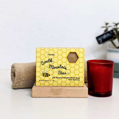 A beeswax candle in a red glass votive, a honey soap, a beech soap dish, and a cotton washcloth.