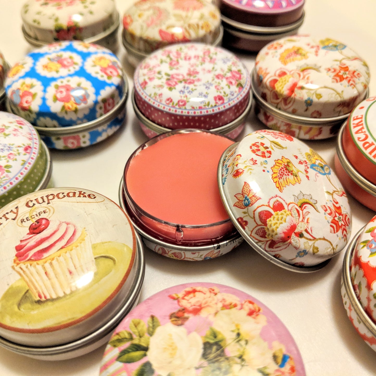 Colorful printed tins filled with light red lip balm. A lip gloss and lip balm in one.