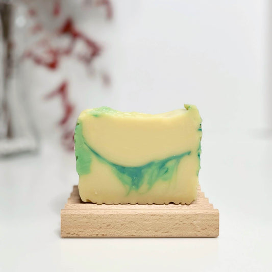 Handcrafted rosemary honey soap with green mica swirls, on a creamy off-white base. The soap rests on a beechwood soap dish.
