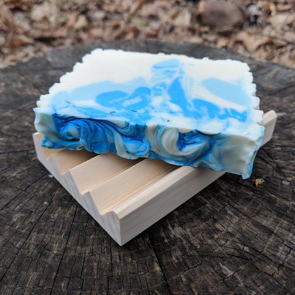 Soap with blue swirls rest on wooden dish on a a tree stump.