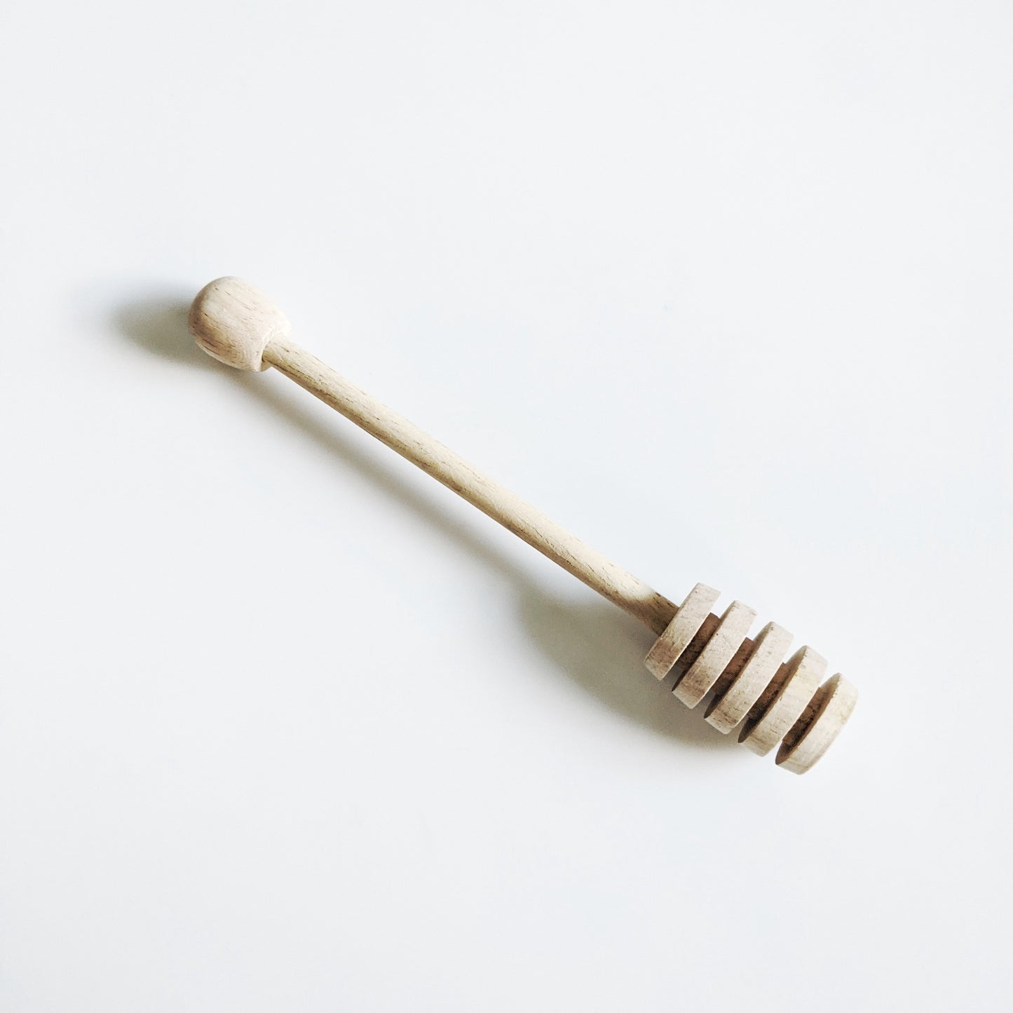 A traditional wooden honey dipper with a grooved top to collect honey. 