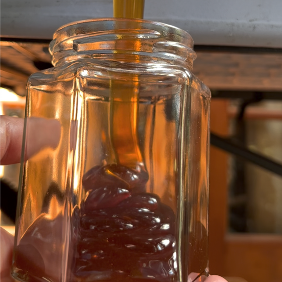 Rich dark honey pours into a glass jar.